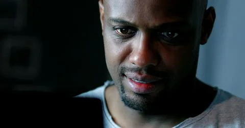 Close-up black man face looking at computer screen at night 写真素材