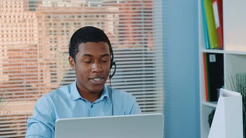 Close-up of black man in headset speaking with somebody and working on the Stock Footage 124251273