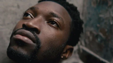Close Up of Black Man Sitting in Worn Bathroom, Gazing Upward in Reflection Vídeo Stock 329581344