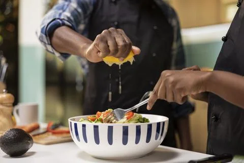 Close up of black man squeezing lemon juice over vegetables in a bowl Fotos Stock