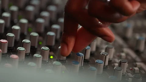 Close-up of Black man's hand adjusting audio mixer knobs on sound console Video stock 331417949