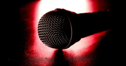 Close up of black microphone on a red light and black background. Stock Photos