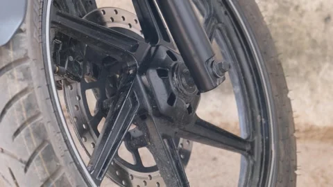 Close-up of a black motorcycle front wheel featuring a disc brake system Видео 329370052