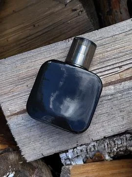 Close up black perfume bottle sitting on dry rustic timber Stock Photos