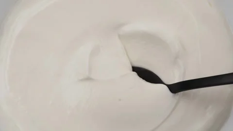 Close-up of a black spoon dipping into thick white yogurt or cream. Background Stock Footage 318464642