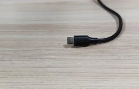 Close-up of a black type-c charging cable on a wooden table background. Stock Photos