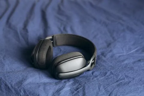 Close up of black wireless over ear headphones on blue bedding. Stock Photos