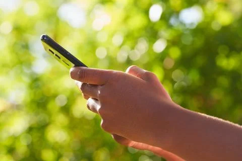 Close up of Black woman's hands using mobile phone, texting in nature leaf bokeh Stock Photos