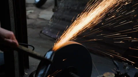 Close up of blacksmith sharpening flat piece of steel against sharpening wheel Stock Footage 147371150