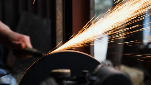 Close up of blacksmith sharpening flat piece of steel against sharpening wheel Stock Footage 147371328