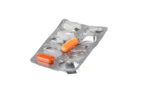 Close-up of a blister with two orange tablets on a white background. Stock Photos