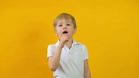 Close up of blond boy keep secret and looking at the camera over yellow Stock Footage 123332277