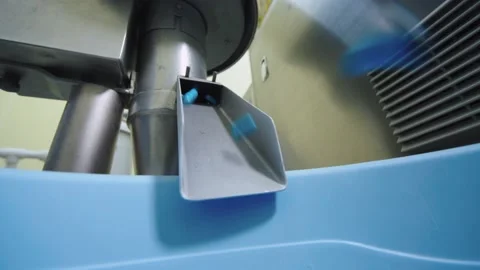 Close-up of blue capsules falling down to the container from automated Stock Footage 200856408