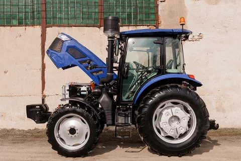 Close up of a blue farm tractor with engine hood raised for repair in a brigh Stock Photos