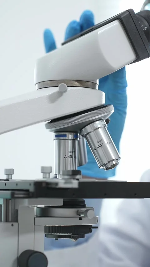Close up of blue gloved scientists hand adjusting microscope in modern Stock Footage 316497515