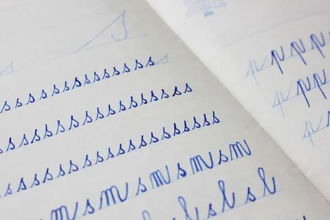 Close-up of blue letters written in cursive by a child in a paper notebook Stock Photos