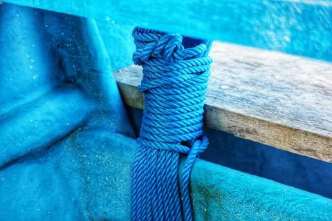 Close up of blue rope coiled and tied around a wooden beam on a weathered blu Stock Photos