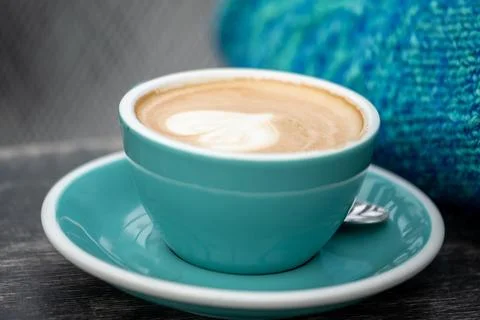 A close up ,blue, steaming cup of latte with artful foam, a heart, in a teal cup Stock Photos