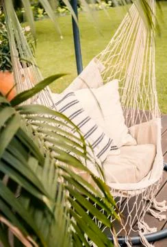 Close-up of a boho hammock hanging in a sunny garden with a palm tree and gre Stock Photos