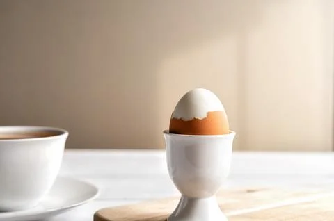 Close-up of a boiled egg in a white ceramic egg cup with cup of tea and with Stock Photos