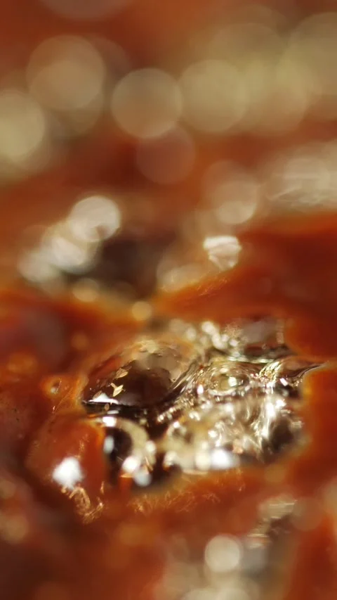 Close-up of boiling thick dark liquid with bubbles and glossy surface. Shallow Stock Footage 304465228
