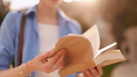 Close up of book in woman’s hands, pages flipping quickly outdoors in sunlight Stock Footage 316295641