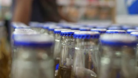 Close up of bottles row with blue caps in a big supermarket with a man walking Stock Footage 166549137