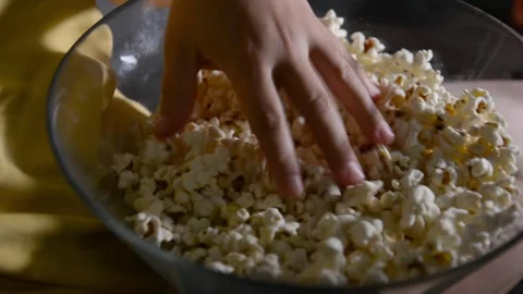 Close up of a bowl filled with popcorn while a hand repeatedly reaches 動画素材 336900398