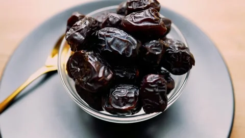 Close-up of a bowl of fresh dates on a dark plate with a golden spoon Stock Footage 320727787