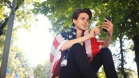 Close up boy with American flag using mobile phone smile sitting on skate in Stock Footage 92048379
