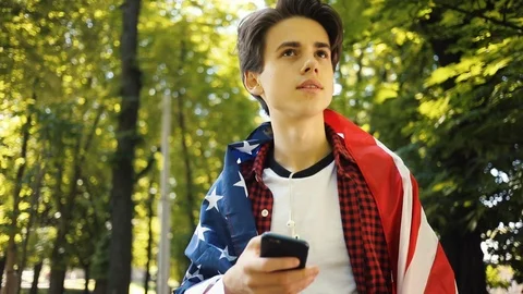 Close up boy with American flag using a mobile phone smile walk happy sunshine Stock Footage 92048758