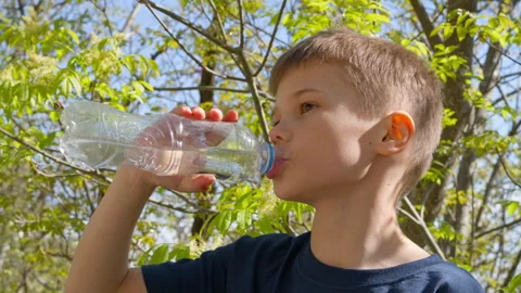 Close-up of boy drinking water from bottle, healthy hydration in spring nature Stock Footage 308032106