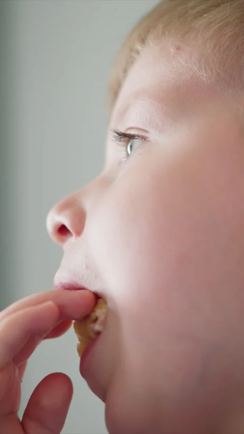 Close up boy eating small food pieces with hand visible plain background with Stock Footage 344794727