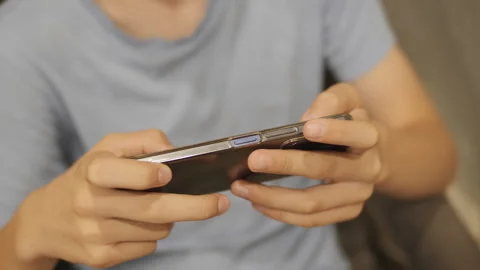 Close-up of a boy holding a mobile phone and typing on the screen Stock Footage 247482997