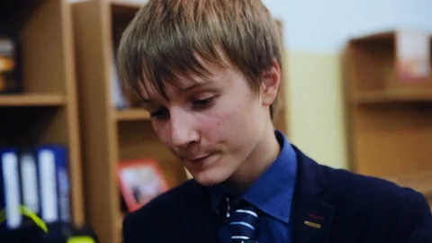 Close up of a boy looking in a backpack talking in a classroom school education Stock Footage 99255903