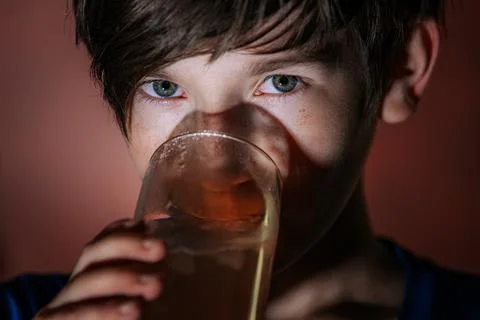 Close-up of a boy with piercing eyes drinking iced tea from a glass. Stock Photos
