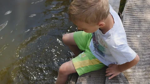 Close up of a boy sitting on bridge with his feet in the lake Video stock 151211114
