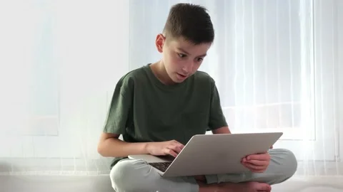 Close up of boy sitting in kitchen typing on laptop Stock Footage 224467186
