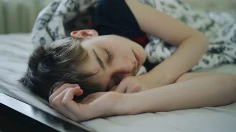 Close-up of a boy sleeping sweetly on a bed under a blanket. Good rest Видео 154370103