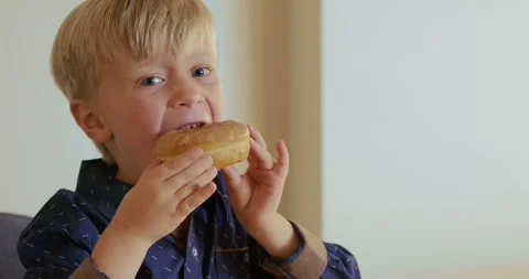 A close-up of a boy smelling a donut glazed with beige chocolate. The boy is at Video stock 347028728
