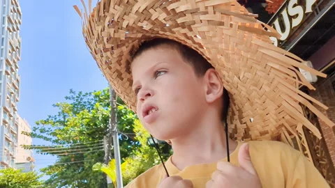 Close up of boy in a straw hat. Hot day in tropics. Video stock 256136824