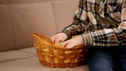 Close-up of a boy touching and picking up Easter colored eggs from wicker basket Video stock 169823121