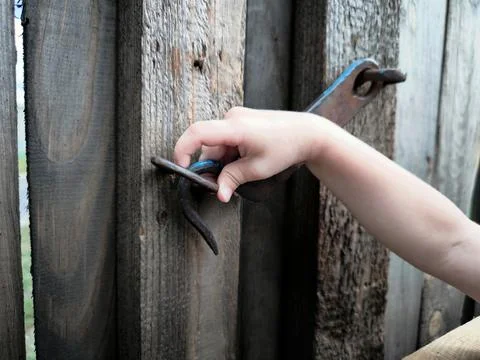 Close-up: the boy's hand opens the iron gate. Stock Photos