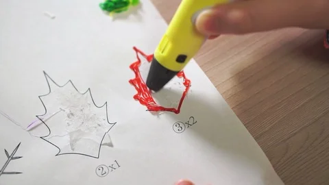 Close-up boy's hand uses a 3D pen. He creates a plant leaf from red ABS plastic. Stockbeeldmateriaal 100387336