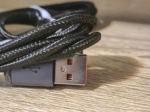 Close-up of a braided USB cable on a wooden surface, showcasing the connector Stock-Fotos