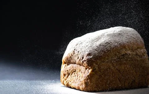 Close up bread with falling flour on black background. Bread making concept. Stock Photos
