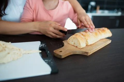 Close-up bread knife and hands of mother and daughter in the kitchen. Stock Photos