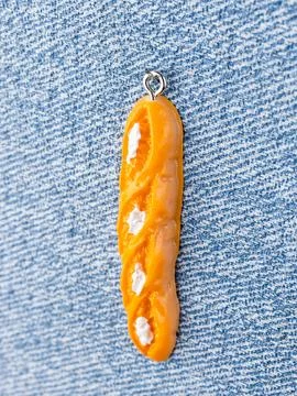 Close-up of a bread roll-shaped pendant for jewelry making, displayed on a bl Stock Photos