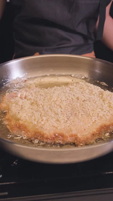 Close-up of breaded pork cutlet frying in hot oil in a stainless steel pan in a Stock Footage 329266369