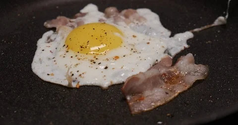 Close-up breakfast preparation, delicious scrambled eggs with fried bacon in pan Stock Footage 120895852